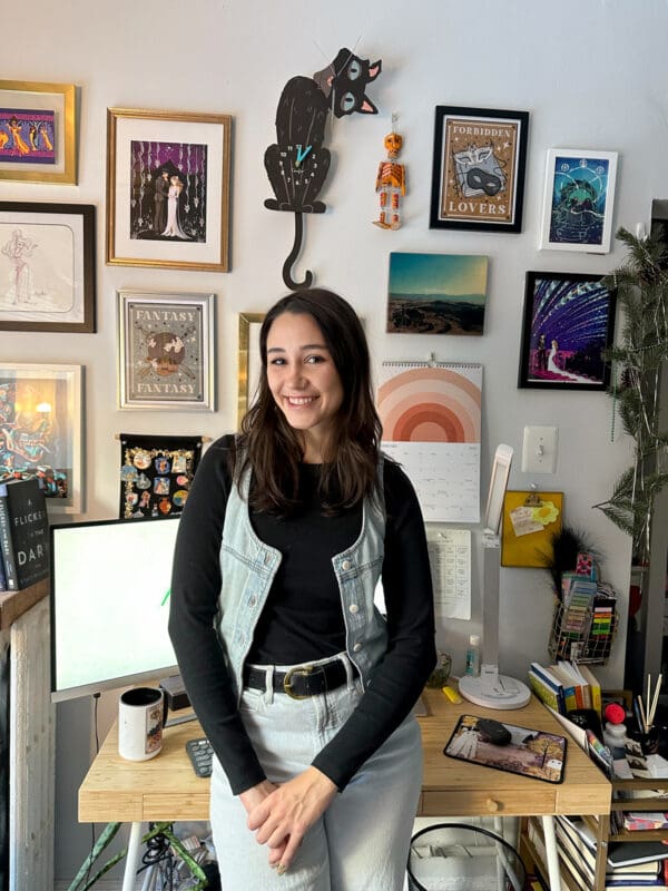Meara poses in front of her work-from-home office, which has art on the walls and a clock shaped like a cat.