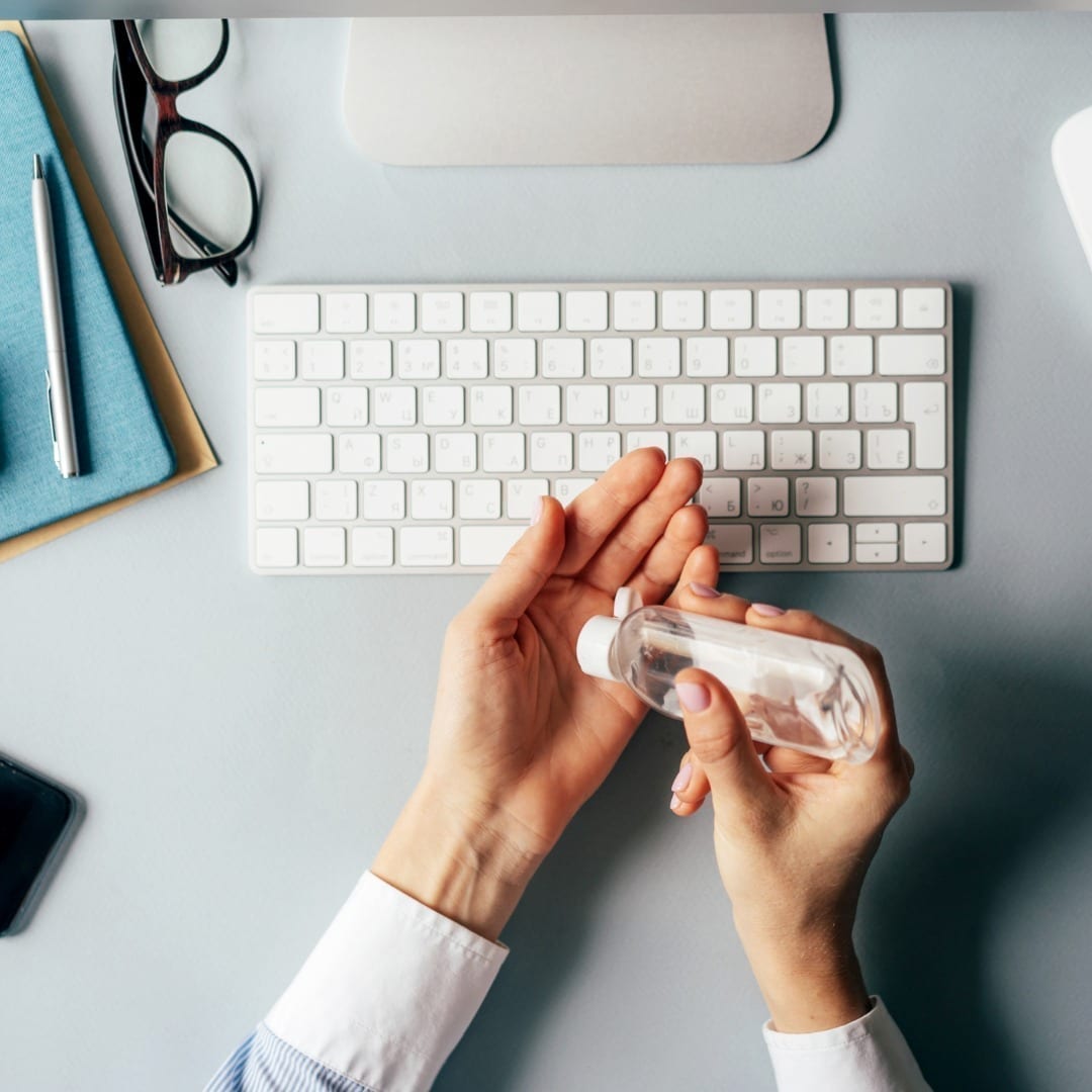 Hands pouring hand sanitizer at desk