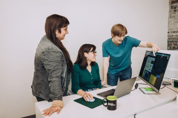 Claire shows a website wireframe to Amanda and Ivey. Ivey indicates something in the design with a smile.