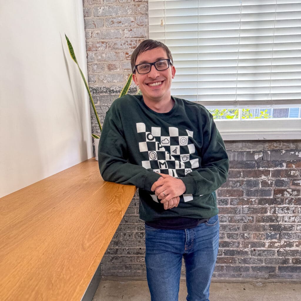 Flynn stands and smiles in the New Orleans office. He's wearing a branded Online Optimism sweatshirt.