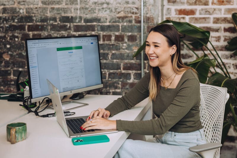 Meara smiles while preparing a Google Looker Studio report on her computer in the office.