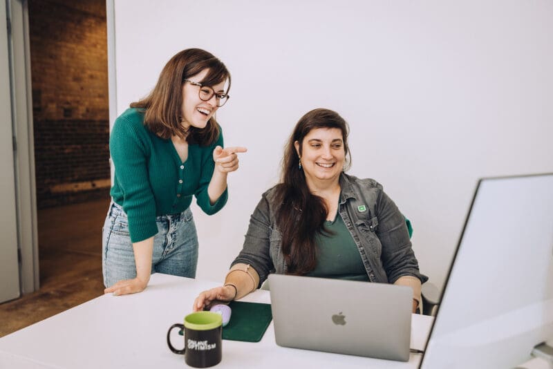 Claire points to something on Amanda's screen and both smile.
