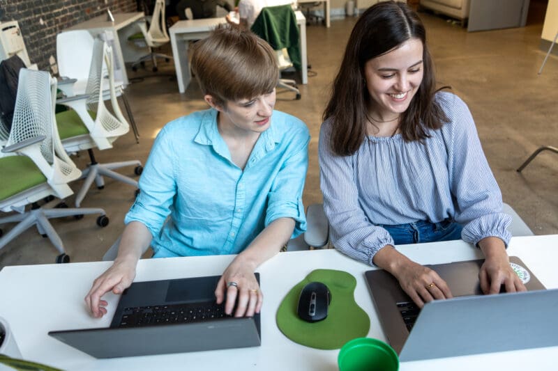 Ivey leans over Claire's laptop to see something on her screen.