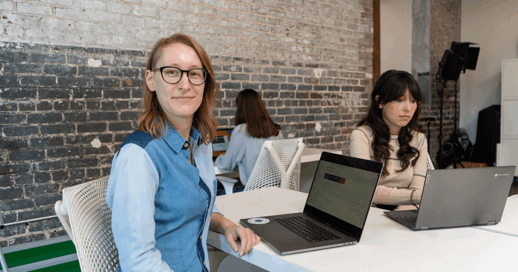 Lauren, who has a Google Analytics page open on her laptop, turns to smile at the camera as Jordan and Claire work on their own projects in the background.