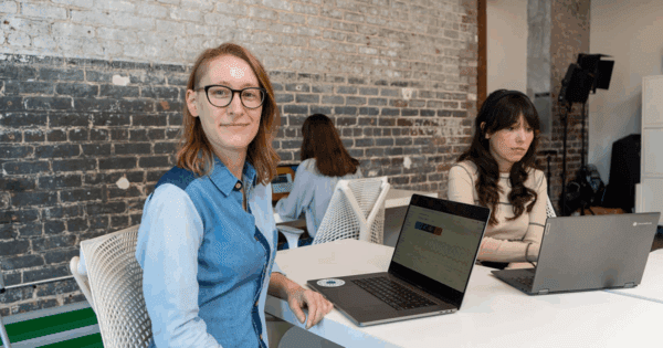 Lauren, who has a Google Analytics page open on her laptop, turns to smile at the camera as Jordan and Claire work on their own projects in the background.