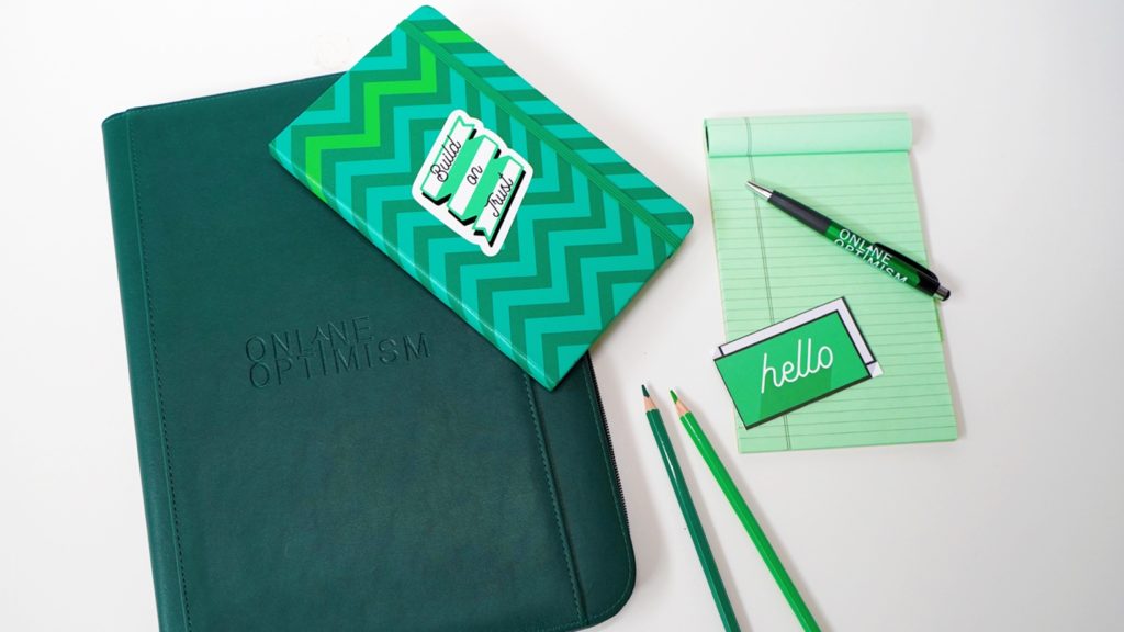 Green notebooks, pencils, a pen and a business card on a white table