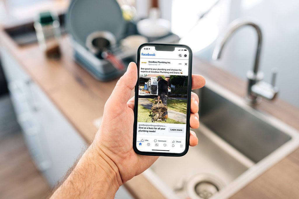 Man looks at a Facebook ad from Goodbee Plumbing while standing over kitchen sink