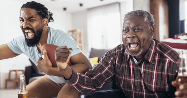 A father and son yelling enthusiastically while watching the football game, demonstrating the importance of having a winning 2025 Super Bowl marketing strategy