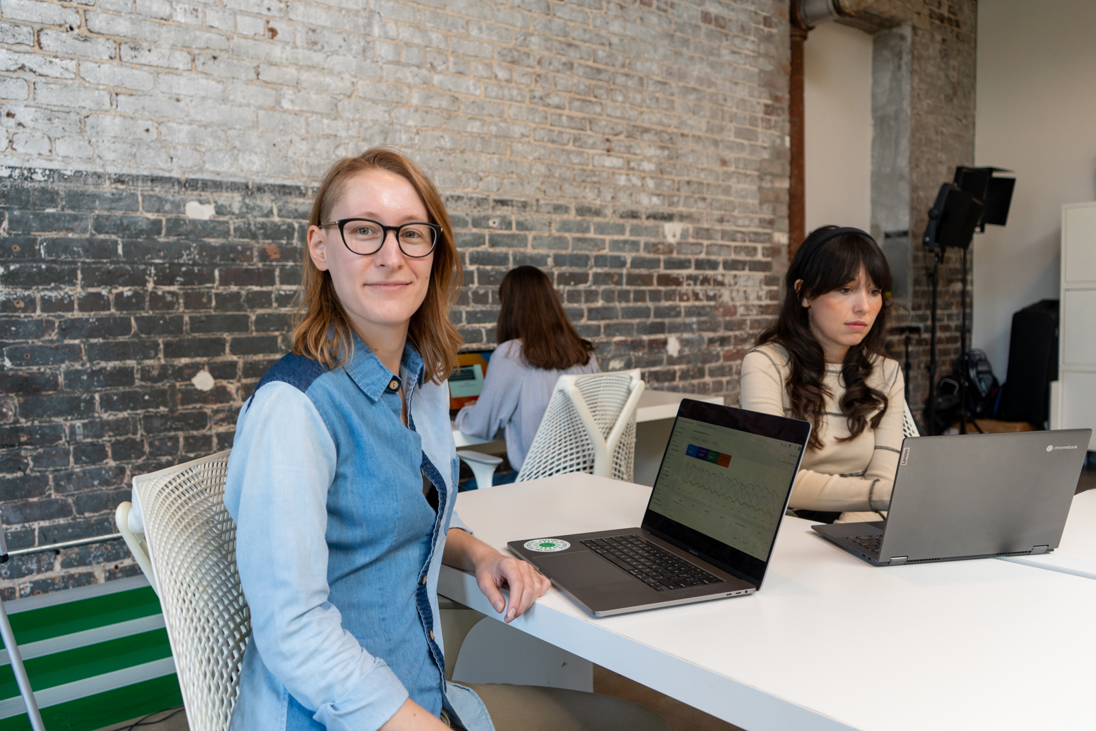 Lauren, who has a Google Analytics page open on her laptop, turns to smile at the camera as Jordan and Claire work on their own projects in the background.