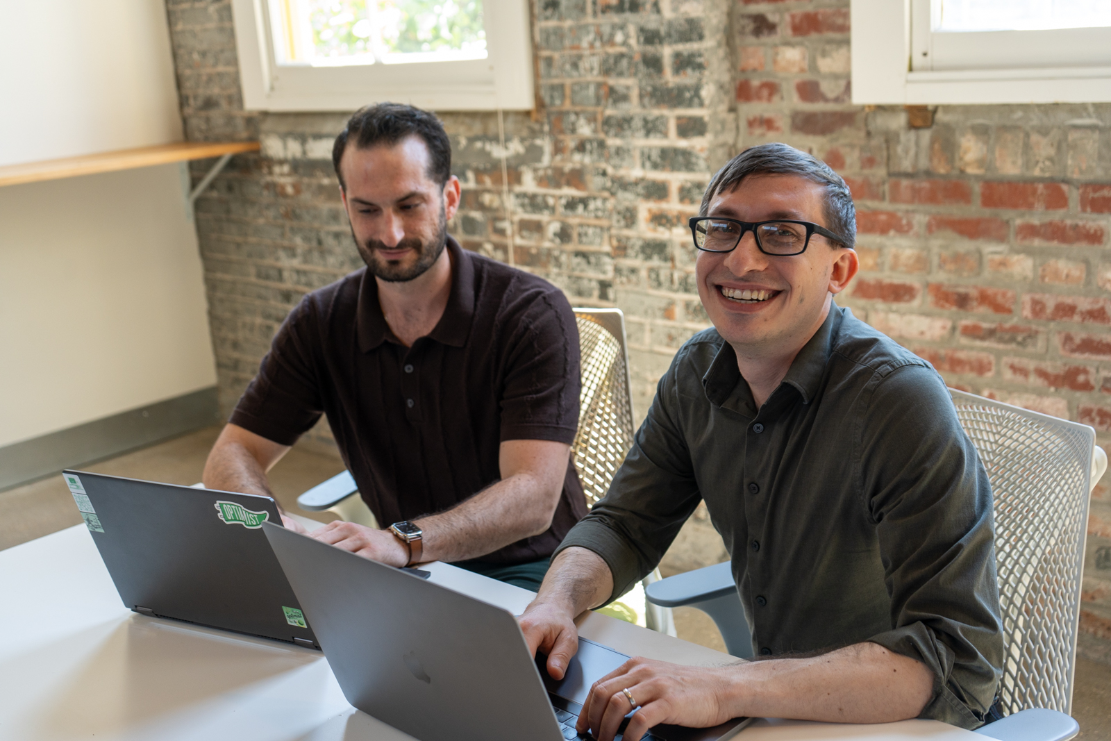 Flynn Zaiger Smiling and Working next to Sam Olmsted on laptops in the Office