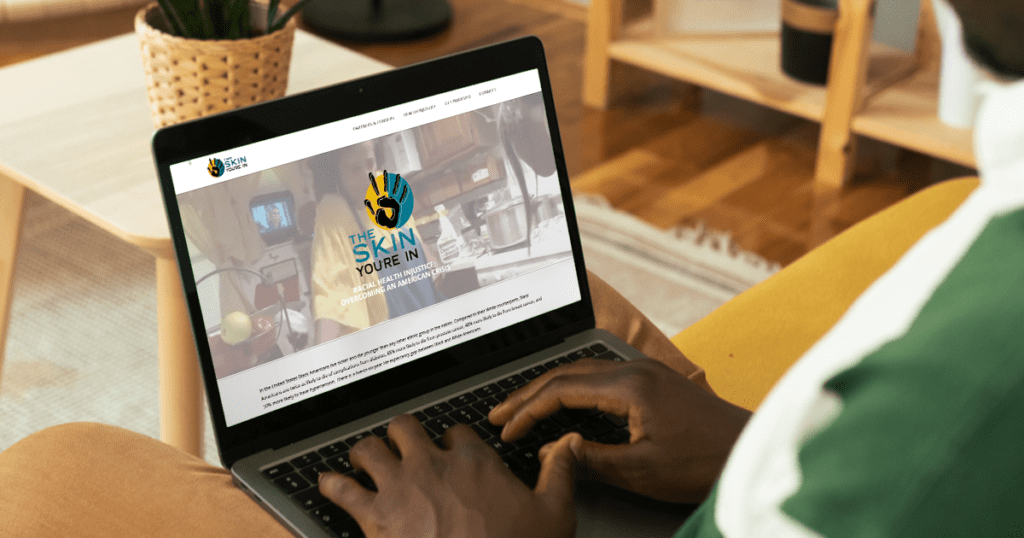 A person browses the "The Skin You're In" website in a warm, well-lit living room.