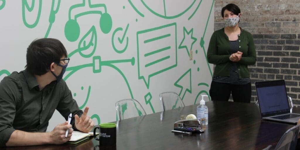 Flynn Zaiger Talking to Sara Bandurian with Masks on in a Conference Room
