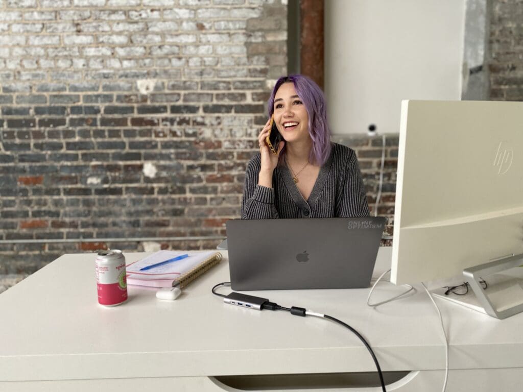 Meara answers her phone with a smile while sitting at her desk in the Online Optimism office.