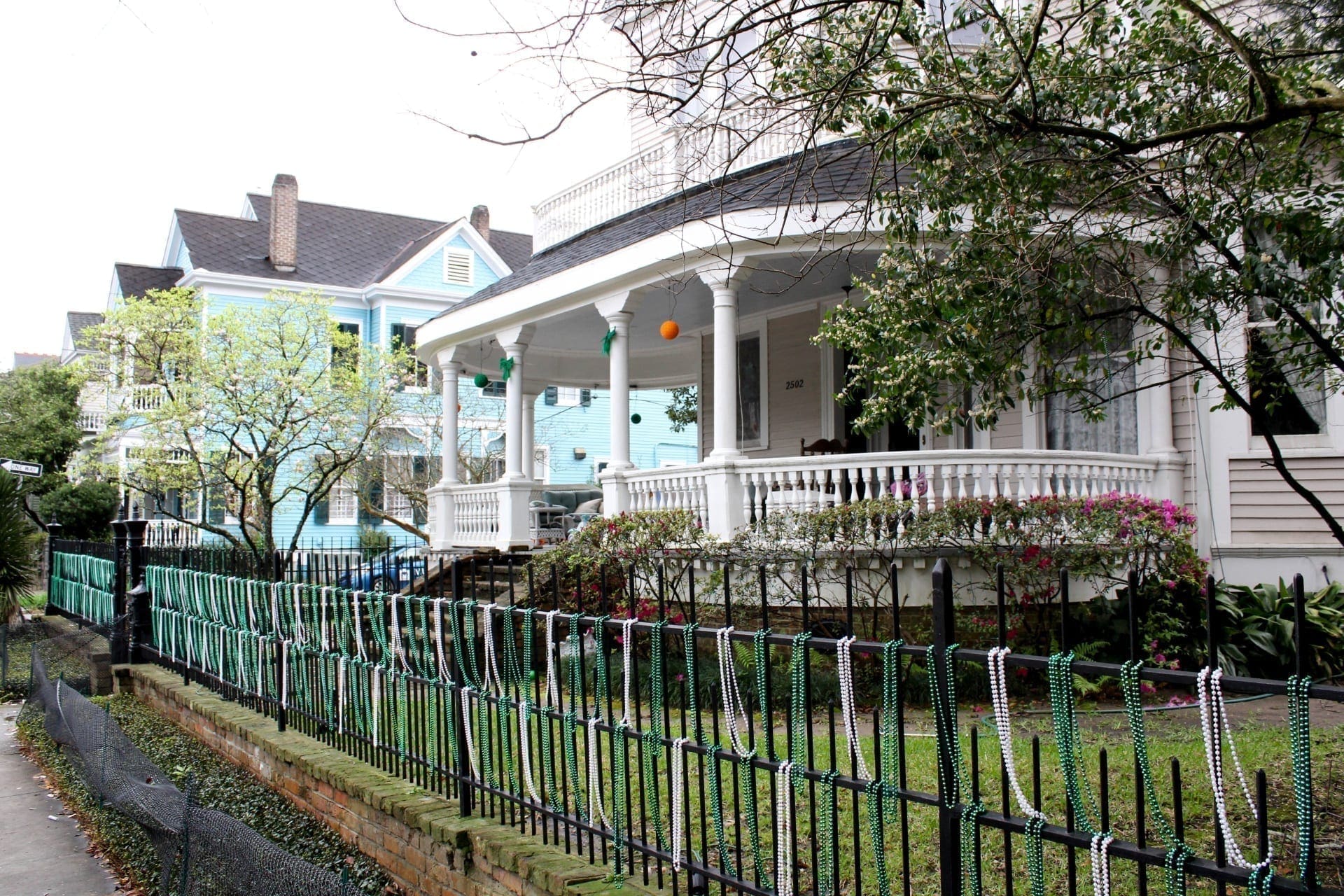 Green and white Mardi Gras beads hung from the fence around a New Orleans house.