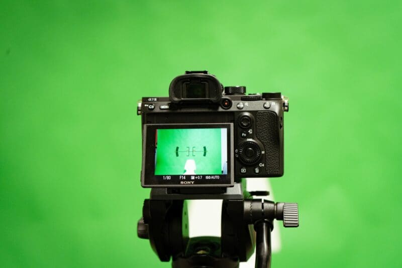 A camera facing a green backdrop with a paper cutout set against it for framing.