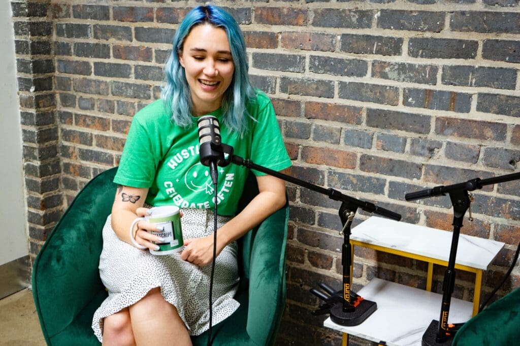 Meara talks into a microphone while holding an "Online Offscript" mug advertising the Online Optimism podcast.
