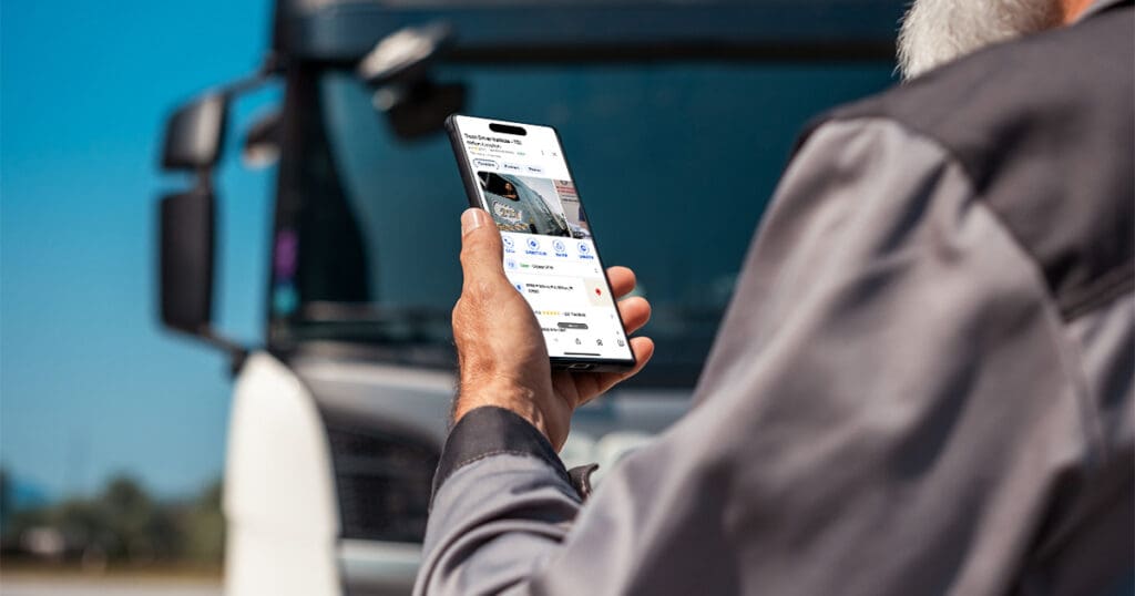 A truck driver looking at TDI's Google Maps location on their phone, outdoors next to their truck.
