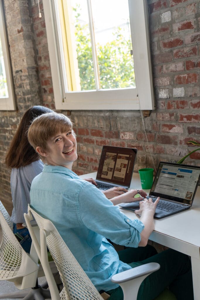 Ivey glances back at the camera with a smile, working beside Claire at the Online Optimism office.