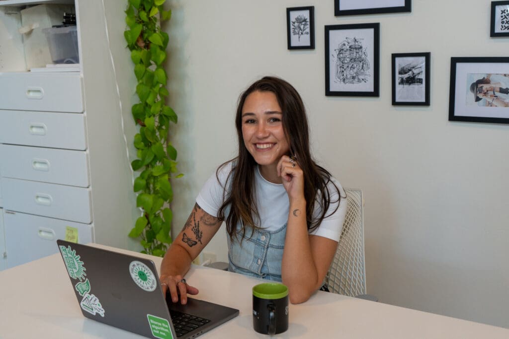 Meara sits at her laptop in the office and smiles at the camera.
