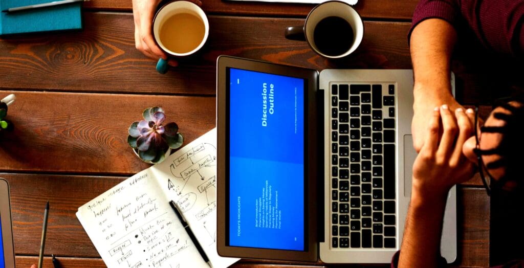 People at a table looking at a laptop with notes and coffee