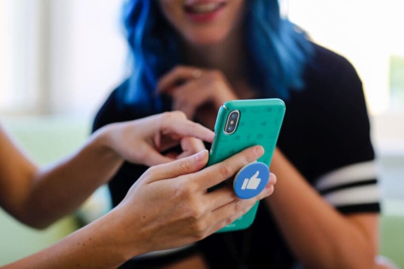 A person holding a phone with a Facebook-style thumbs-up emoji on its back.