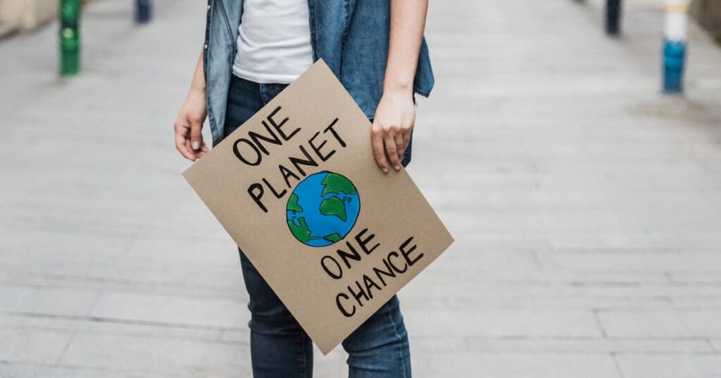 A person holding a cardboard sign with the earth painted on it and the slogan "One Planet, One Chance".