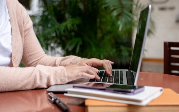 A person in a pink sweater typing on a laptop.