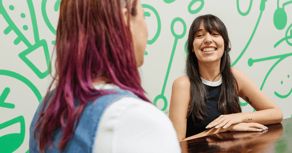 Jordan and Madi chat together at the table in the Online Optimism office.