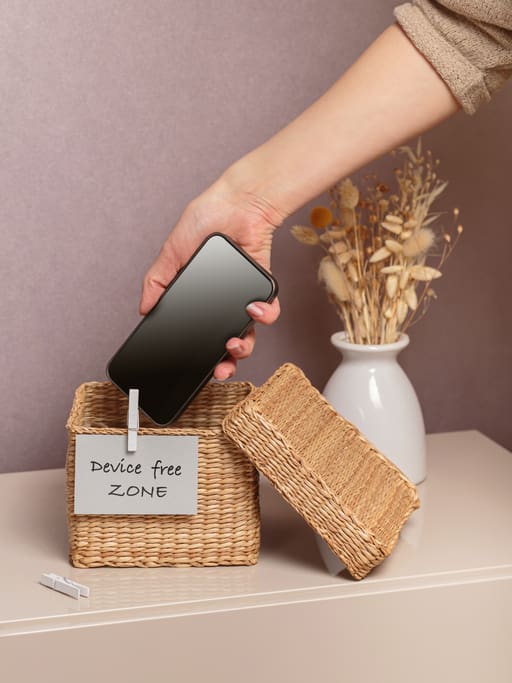 A photo of a person putting their phone inside a box labeled device free zone