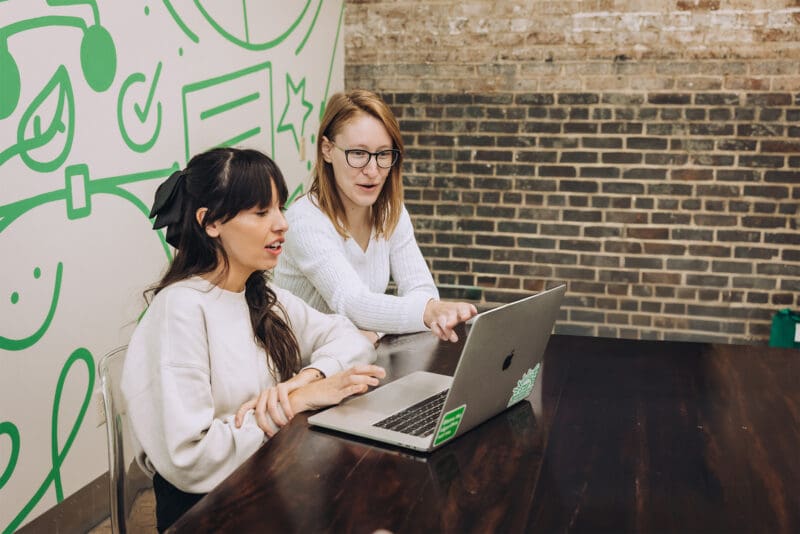 Lauren and Jordan work together on a laptop in the conference room.