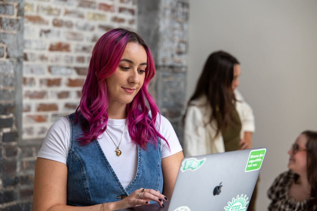 Madison works on a laptop while Optimists converse in the background.