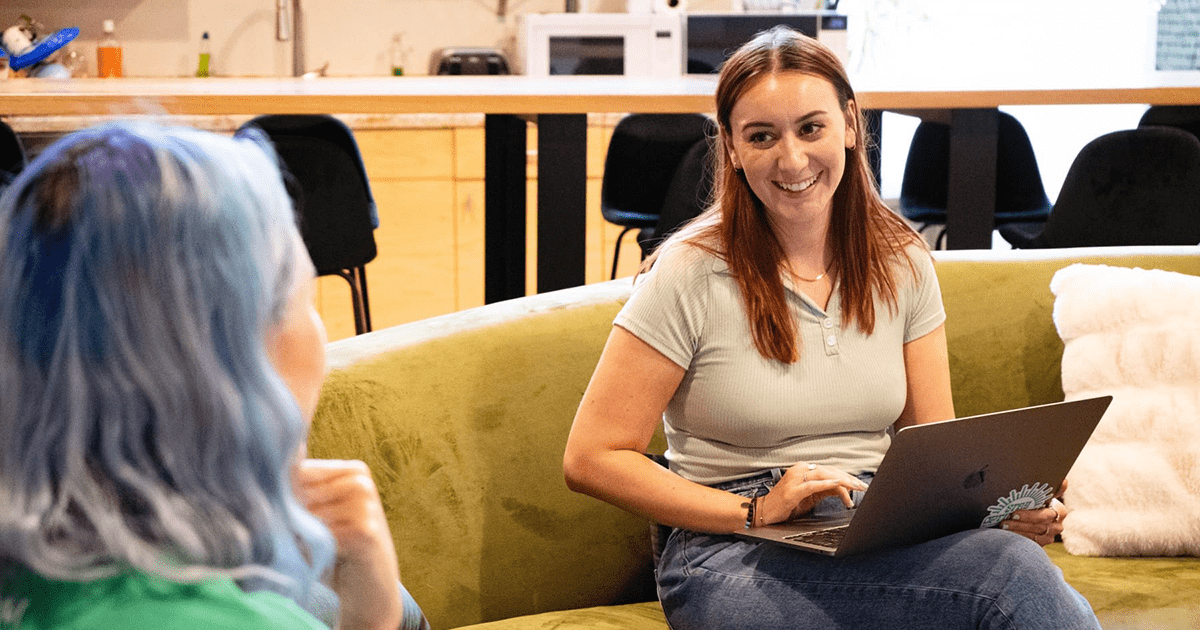 Madison and Meara sit together on the couch at the Online Optimism office, deep in conversation.
