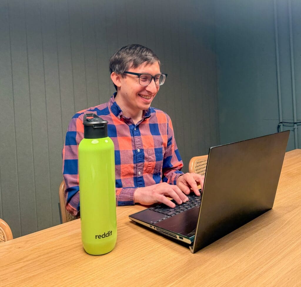 Flynn smiling with Reddit water bottle and laptop.