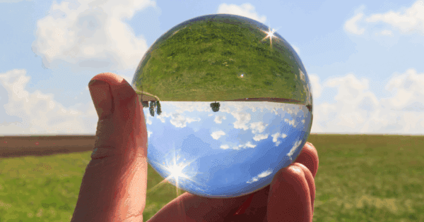 Hand holding a crystal ball outdoors in a field. The crystal ball reflects the scene upside down.
