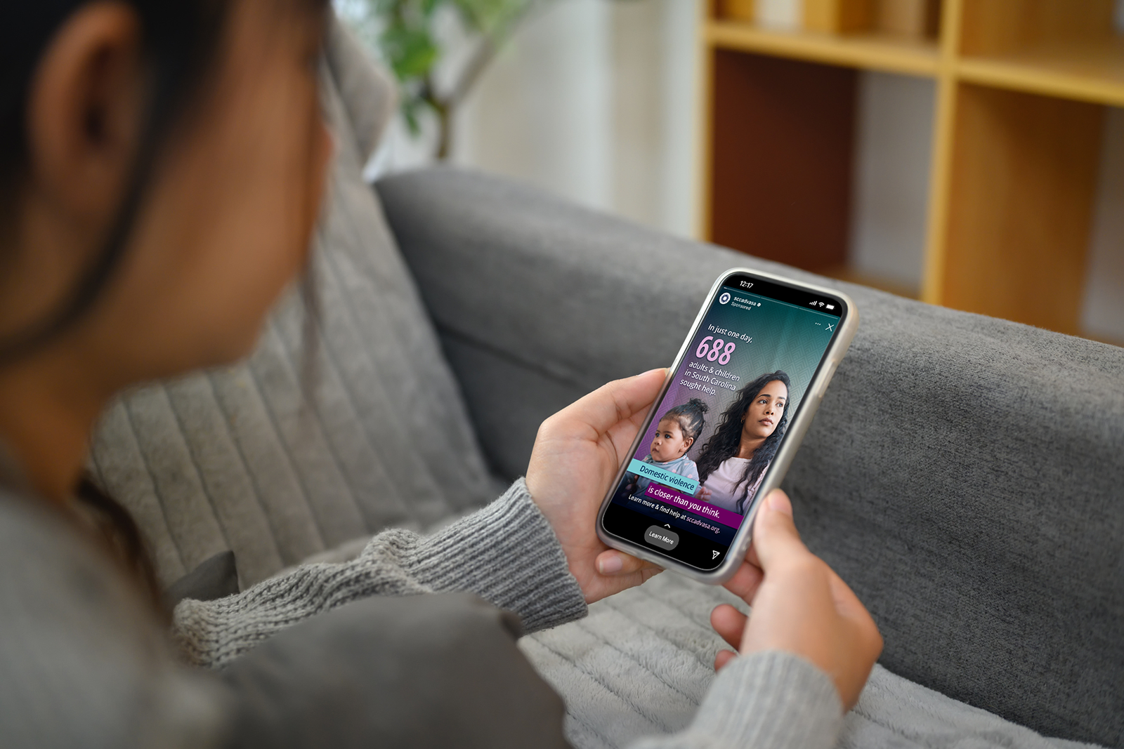 Young woman looks at a SCCADVASA ad on her phone. The ad shows an image of a woman and baby, with the text, "In just one day, 688 adults & children in South Carolina sought help. Domestic violence is closer than you think." With a link to learn more.