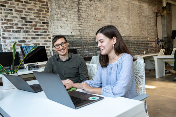 Flynn and Claire work together at a desk on their laptops