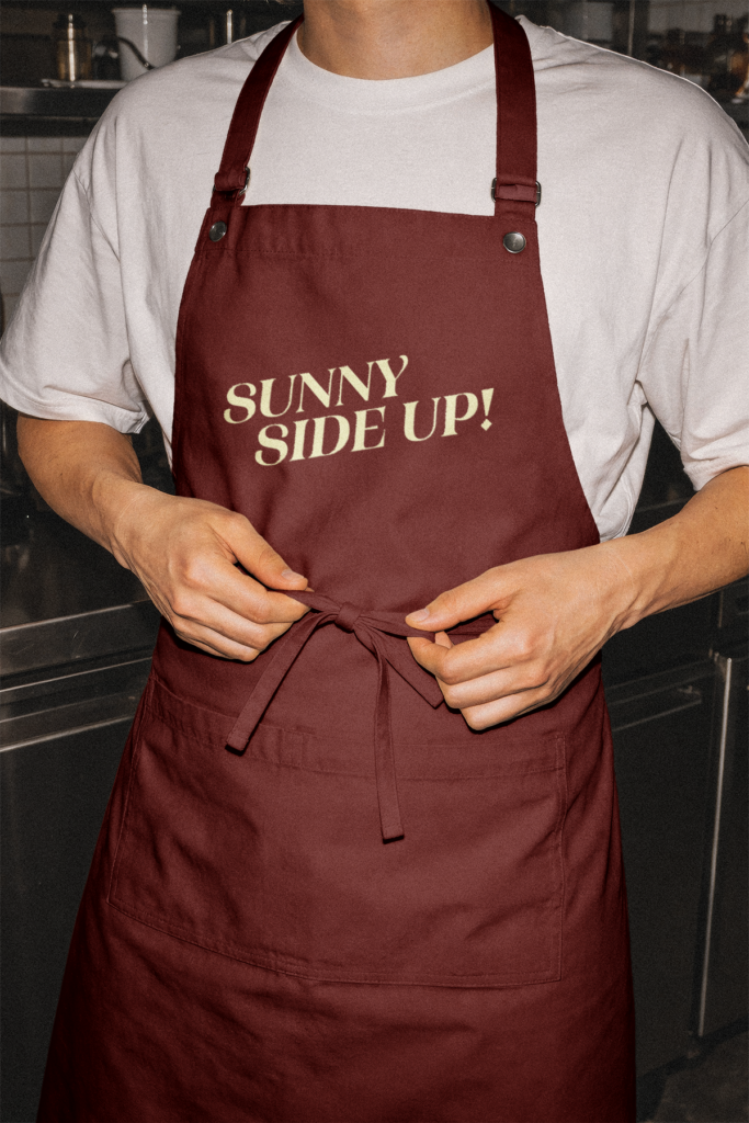 Red apron printed with yellow text that reads 'Sunny Side Up!'