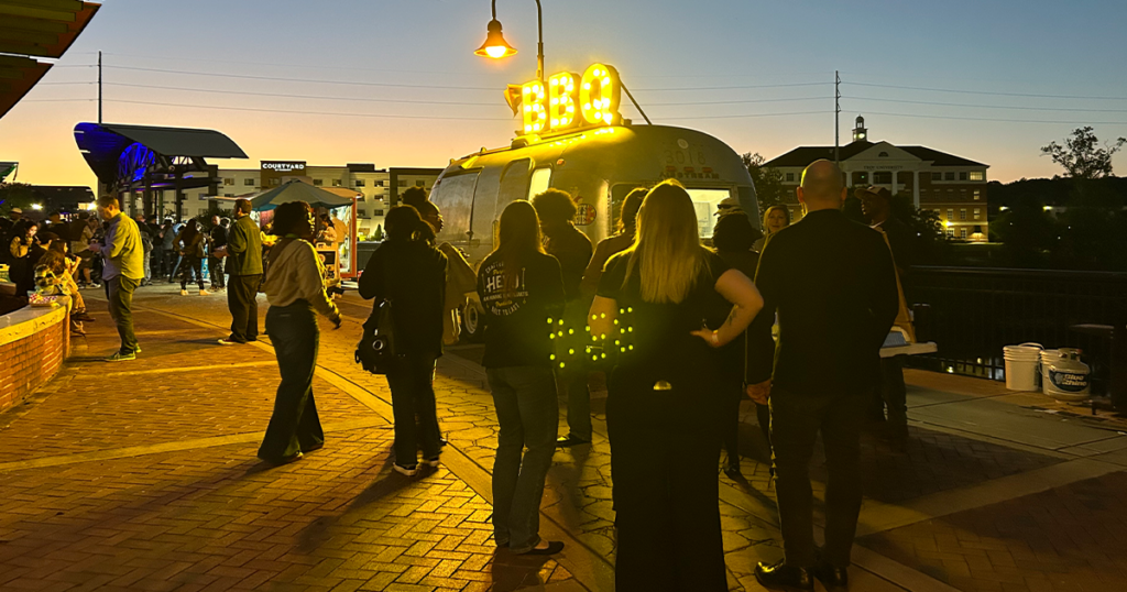 A crowd gathers at sunset around a barbecue food truck.