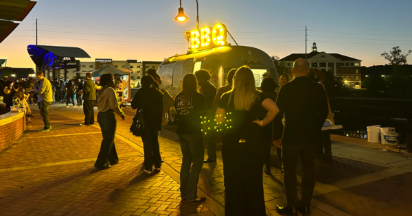 A crowd gathers at sunset around a barbecue food truck.