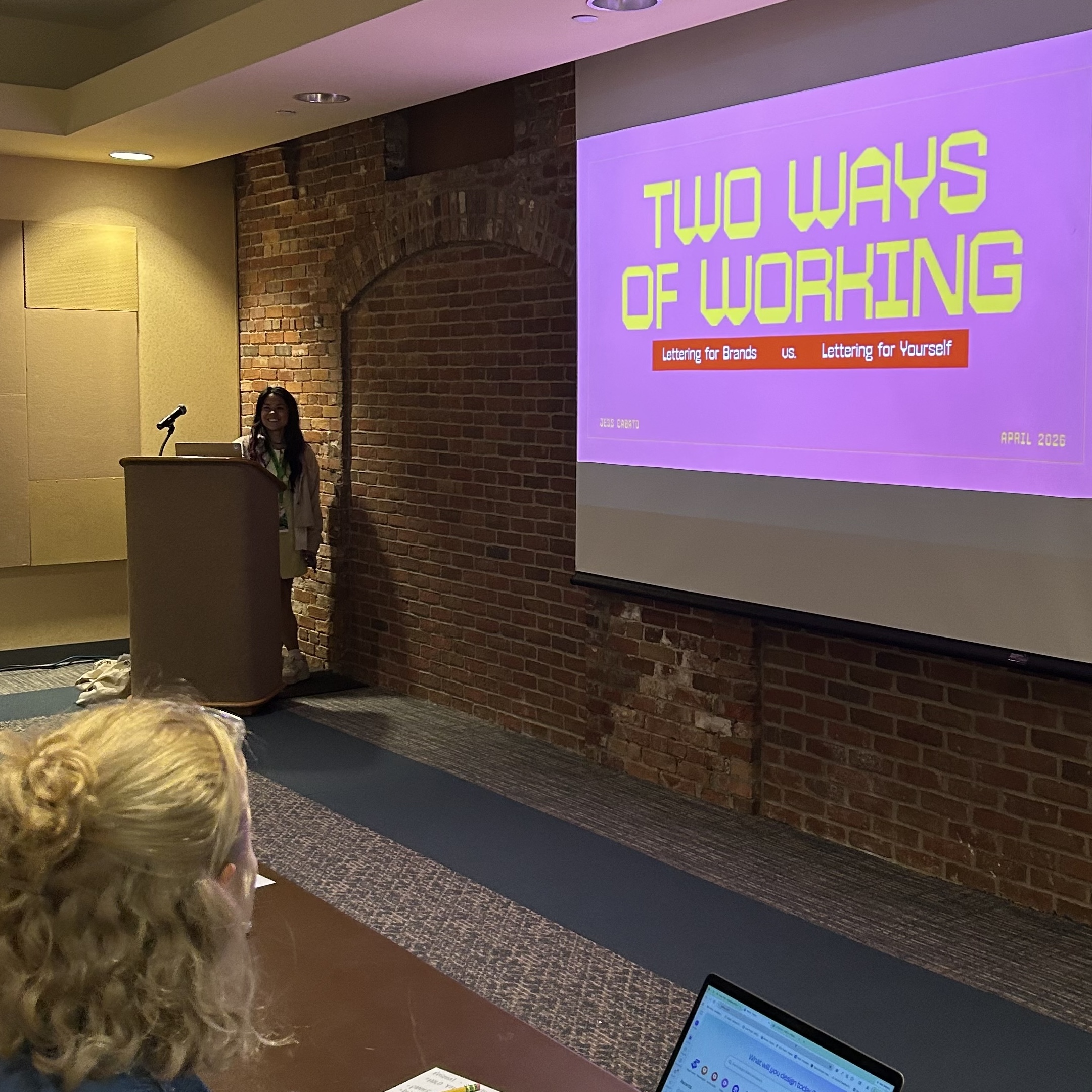 Jess Cabato stands in front of podium speaking during her "Two Way of Working" workshop