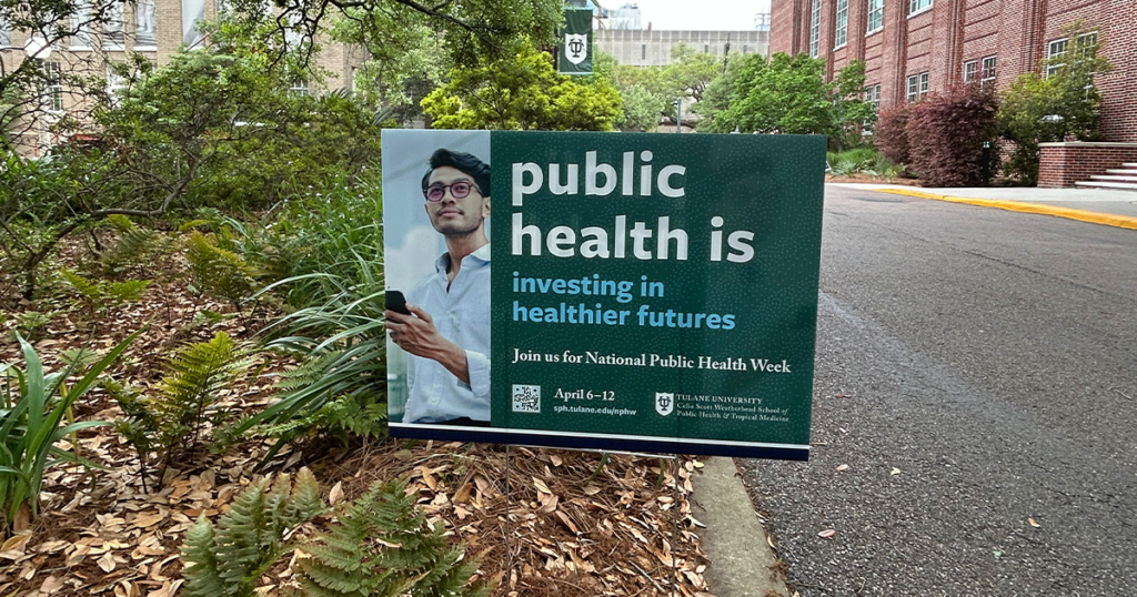 Yard sign on Tulane Campus with text that reads "Public health is investing in healthier futures" with photo of man looking at phone.