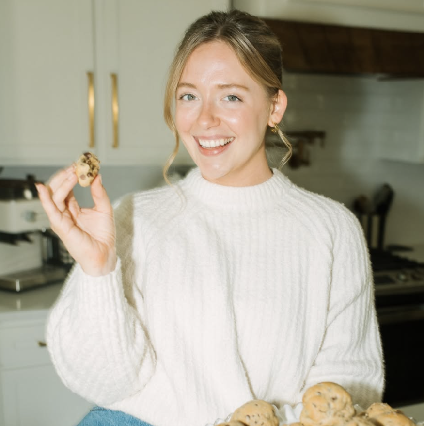 New Orleans influencer Abi Caswell, owner of the bakery Batter, holds up a cookie from a plate with a happy smile.