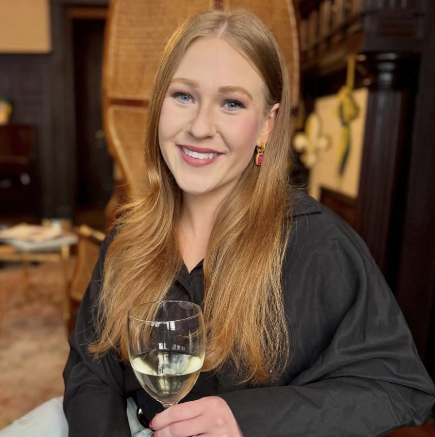 New Orleans influencer Bucket List NOLA (Lauren Womac) smiles at the camera as she holds a glass of white wine.