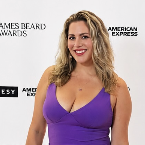 New Orleans influencer Carla Pesono smiles for the camera in a vivid purple dress, posing in front of a branded step-and-repeat background.