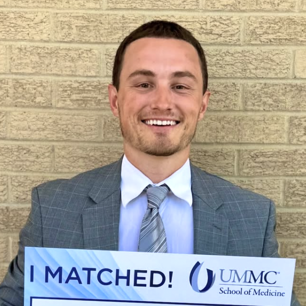 New Orleans influencer Dr. Drewby (Drew Boyd) holds up a sign that says "I Matched! UMMC School of Medicine" with a big smile.