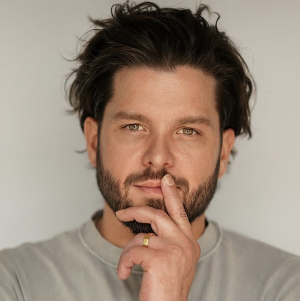 New Orleans influencer Eric Michael Coyle, founder of Aria Hair, leans his chin on his hand and looks at the camera with a thoughtful expression.