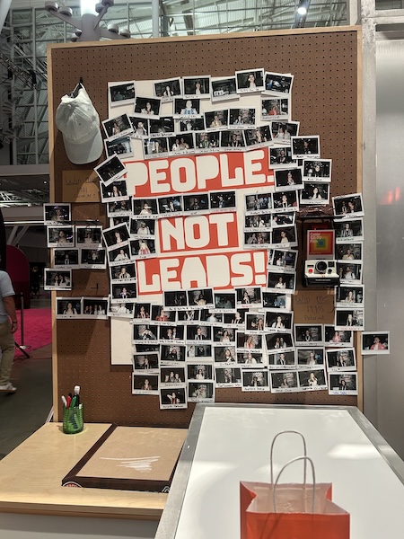 A board at Hubspot Unbound with many instant photographs of people are displayed, along with the words "People, Not Leads!"