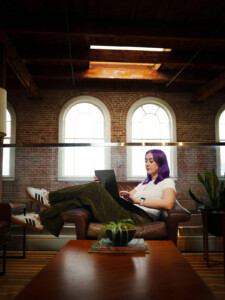 Madison sits in a chair in the office, working on her laptop