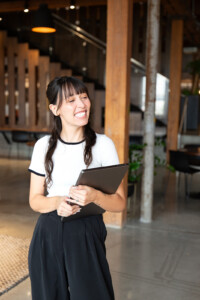Jordan stands in the office, holding her laptop and smiling