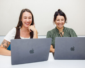 Meara and Sara laugh while working on laptops together